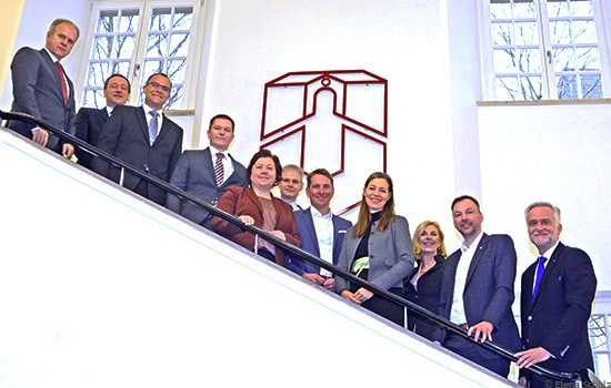 Vertreterinnen und Vertreter von Universität, regionalen Unternehmen, IHK sowie Stadt und Landkreis stehen auf Treppe vor Universitäts-Logo
