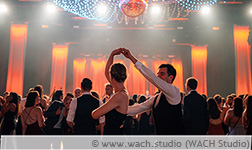 Ein ausgelassenes Tanzpaar beim Uniball 2023 bei einer Drehung vor der hell beleuchteten Bühne des Saals